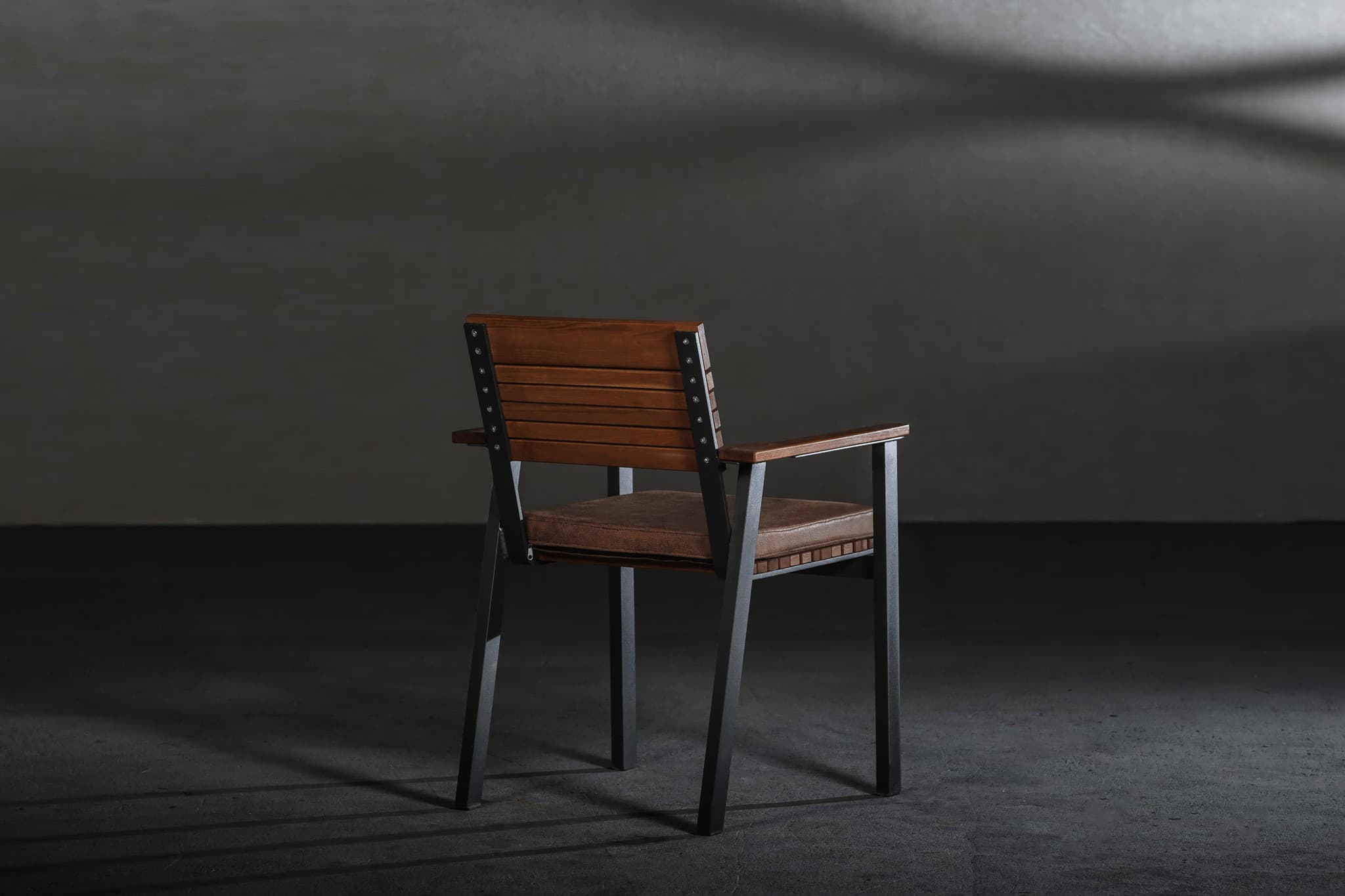 A slatted wooden armchair on a steel frame in a dim concrete room